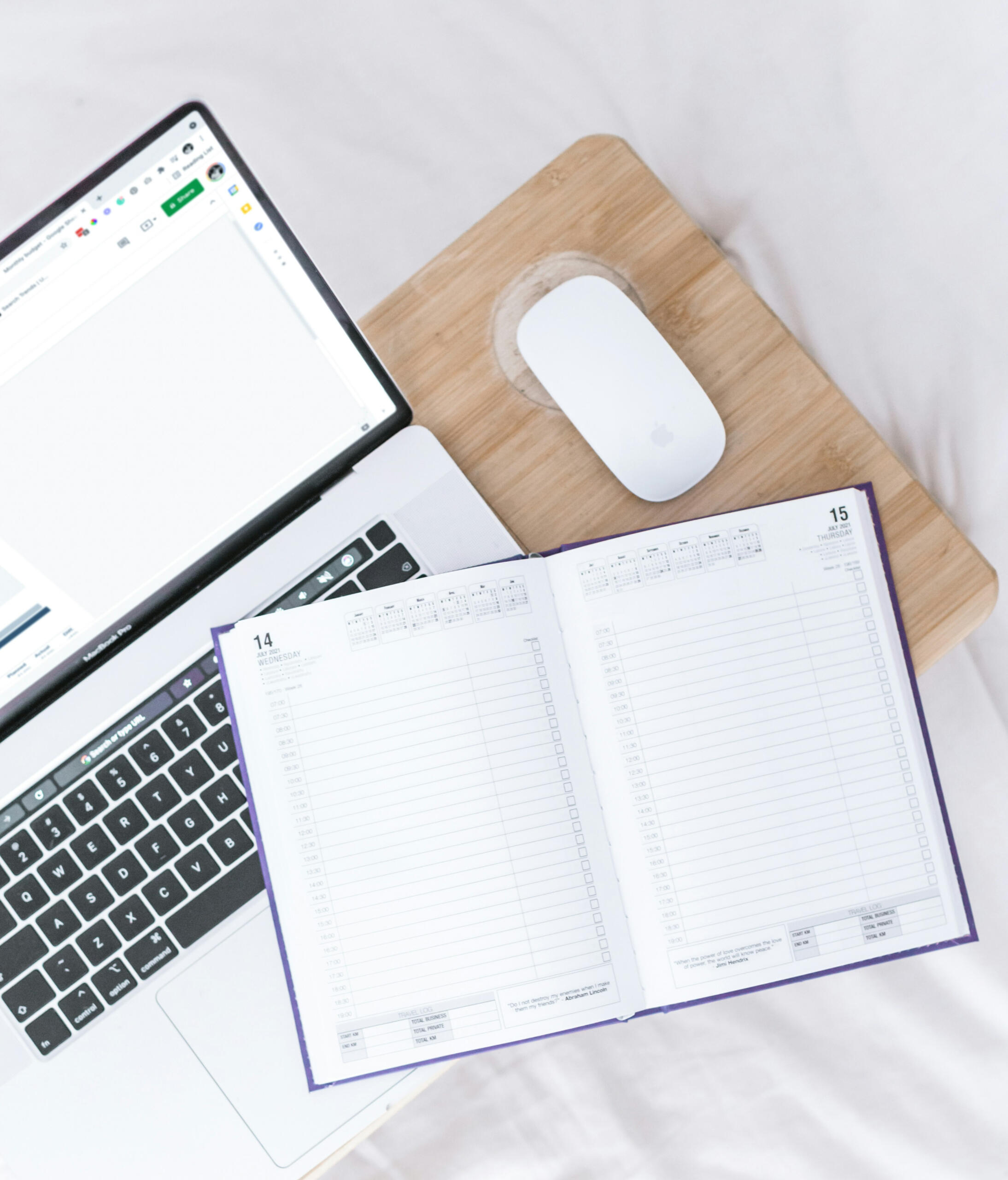 Laptop on desk, with open planner and mouse.